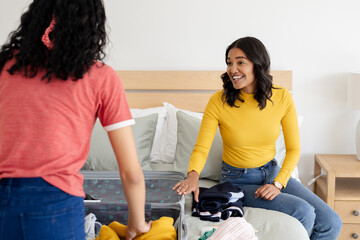 Mother and daughter packing suitcase on bed, preparing for family trip