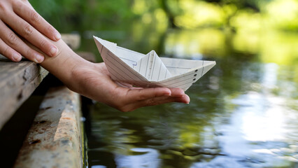 The boy launches a paper boat from the bridge in. water