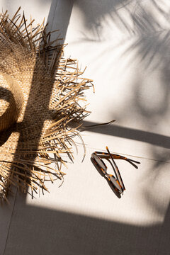 Overhead shot of stylish artisanal straw hat and tortoiseshell sunglasses at a luxury hotel resort with shadows of architectural windows and palm fronds. 
