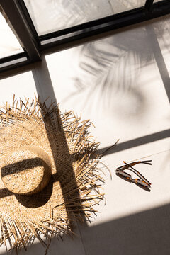 Overhead shot of stylish artisanal straw hat and tortoiseshell sunglasses at a luxury hotel resort with shadows of architectural windows and palm fronds. 