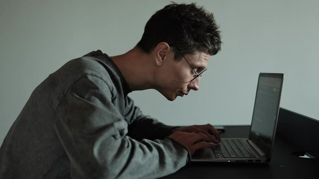 Neck pain from bad posture while using laptop. Freelancer experiencing neck discomfort at Home. Young man in glasses suffering from muscles tension. Gray background