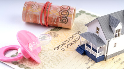 Baby pacifier and 5000 rubles on the table and a model of the house concept of buying a home