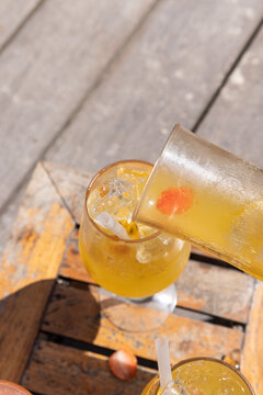 Pouring a fruity sangria from a carafe into a glass during the summer at a restaurant beach club on wood tables. 
