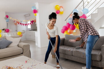 Cleaning living room after party, African American women surrounded by colorful balloons