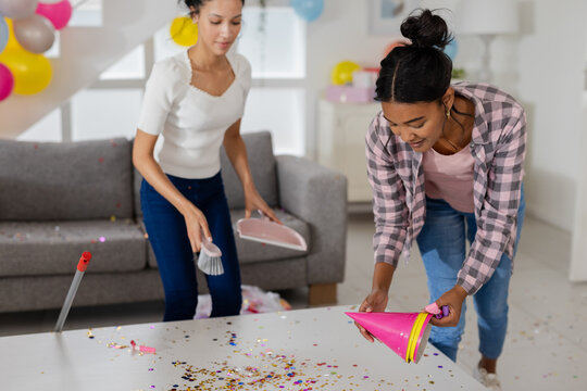 Two women cleaning up party decorations and confetti in living room