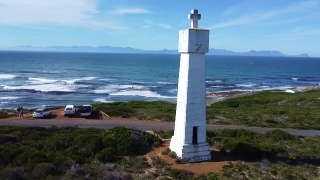 Aerial view of dias cross monument near the coastline with mountains and vehicles parked nearby south africa