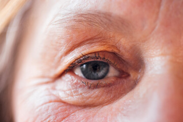 Close-up of an elderly woman blue eye. The face of a mature lady with facial wrinkles and no makeup.