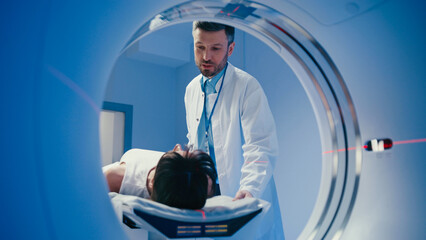 Handsome male doctor raising his hand while explaining something to patient inside of CT tunnel....