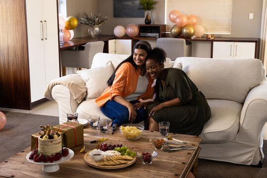 Naklejki Celebration at home, friends laughing and eating snacks and cake on sofa