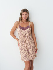 Woman with wavy hair in floral slip dress, featuring purple lace detailing at the top, standing confidently with one hand on hip, against a neutral background, exuding elegance and poise