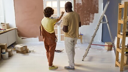 Two individuals discussing and examining color samples for home renovation. Renovation tools, supplies, and ladder visible in room amid ongoing transformation
