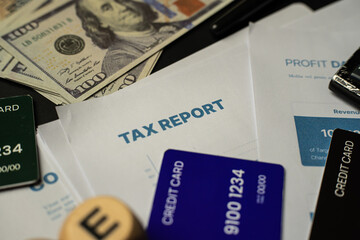 Top view of tax paperwork with "TAX REPORT" headline, American dollar bills, and credit cards scattered on the desk. The scene portrays a realistic representation of annual tax return preparation