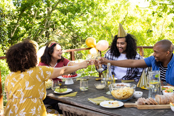 Friends celebrating outdoors, toasting with drinks at festive table with snacks