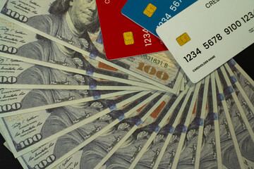 A visually striking composition showing multiple $100 US dollar bills fanned out beneath three colorful credit cards. Ideal for content related to financial literacy