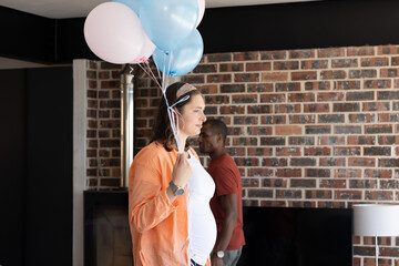 Celebrating at home, pregnant woman holding balloons with family around her