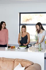 Selbstklebende Fototapeten Preparing salad together, friends cooking and chatting in modern kitchen © wavebreak3