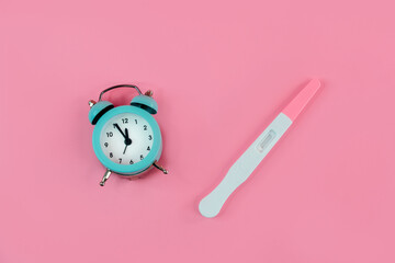 Alarm clock and pregnancy test on pink background, Female fertility biological clock concept, Women's health and fertility