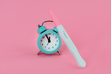 Alarm clock and pregnancy test on pink background, Female fertility biological clock concept, Women's health and fertility