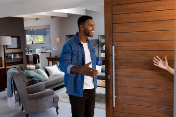 African American man welcoming guest at home, smiling and opening door warmly