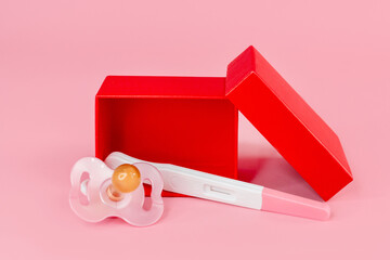 Pregnancy test in a red gift box and a pacifier on an isolated background, the concept of waiting...