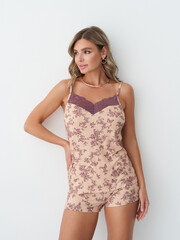 Woman in floral-patterned beige romper with lace detail, stands with hand on hip, gazing to the...