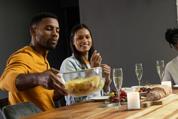 Friends enjoying dinner together, sharing food and drinks at festive table