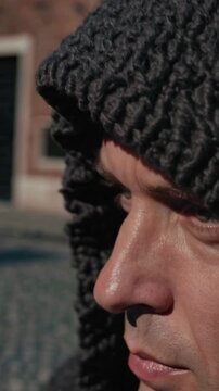 Outdoor Close-Up of Watchful Man in Knitted Hood against Urban Brick Background