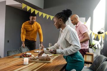 Friends setting table with food and drinks, preparing for festive dinner party