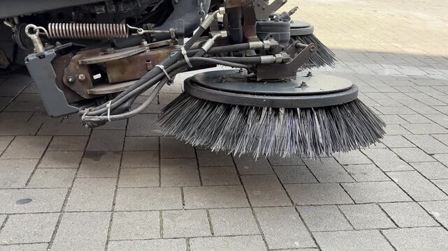 Detailed view of an industrial street sweepers rotating brush system cleaning an urban paved surface with mechanical precision.