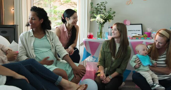 Group of happy multiracial and white female friends with baby taking pictures at a baby shower party