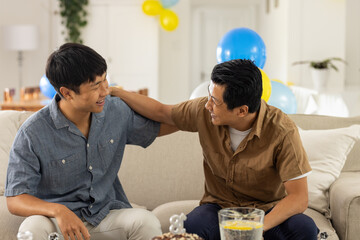 Two men sitting on sofa, laughing and enjoying friendly conversation at home
