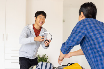 Friends packing suitcase together at home, sharing headphones and smiling