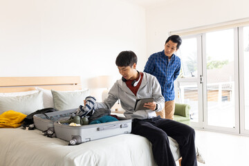 Father and son packing suitcase on bed, preparing for family vacation