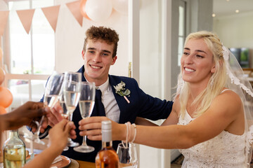 Bride and groom toasting with friends, celebrating joyful wedding reception indoors