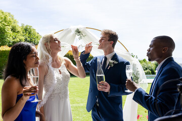 Bride and groom toasting with friends outdoors, celebrating joyful wedding moment