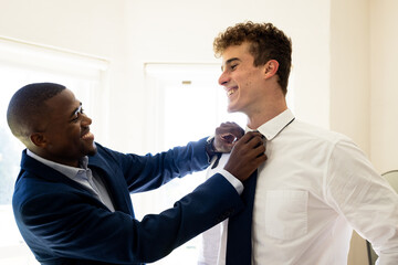 Friends preparing for wedding, adjusting tie and smiling in bright room