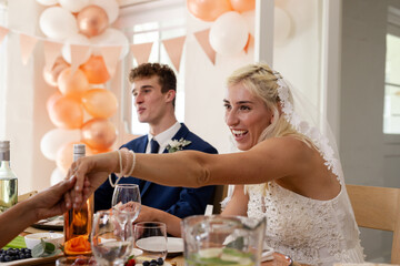 Bride joyfully shaking hands at wedding reception with smiling groom nearby