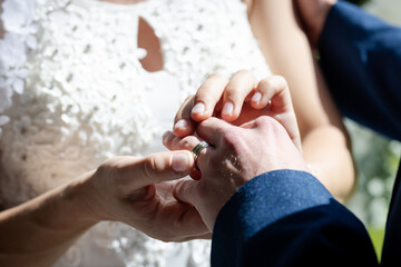 Bride placing ring on groom's finger during wedding ceremony, hands close-up