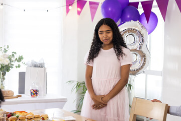 Young girl in pink dress smiling at birthday party with balloons and gifts