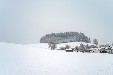 Snow-covered landscape with a hill and farmhouse during winter in a serene rural setting