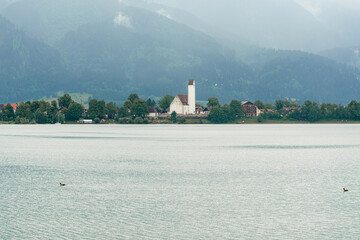 Serene lakeside view with mountains in the background near a quiet village during overcast weather