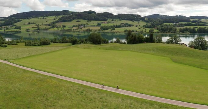 Two Friends Cycling Along Lake Irrsee, Austria &ndash; 4K Wide Drone Aerial Adventure Shot