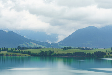 Mountain landscape with serene lake reflecting cloudy sky and lush greenery in the foreground at...