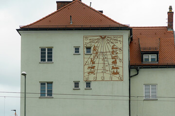 Historic sundial stands prominently on building facade in a European town under overcast sky