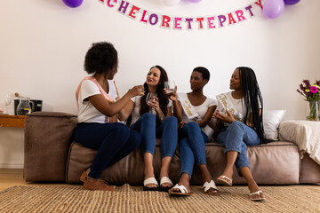 Toasting with champagne, diverse female friends celebrating bachelorette party on couch