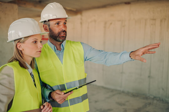 Construction site supervisor explaining blueprint to architect colleague - Powered by Adobe