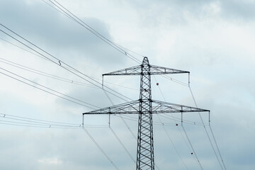 High voltage power lines stretch against a cloudy sky during late afternoon in an industrial area
