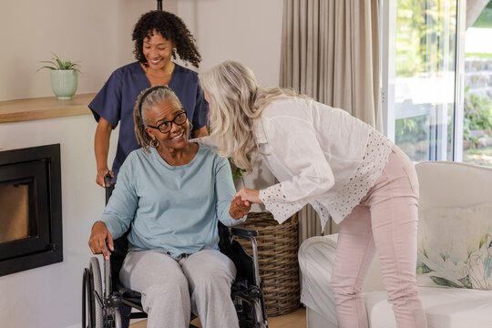 Caregiver assisting senior woman in wheelchair while friend visits at home
