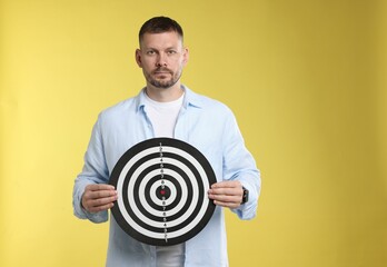 Targeting. Man with dart board on yellow background