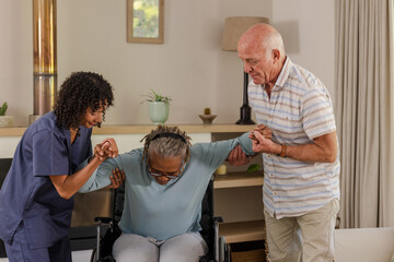 Caregiver and senior man assisting elderly woman from wheelchair at home
